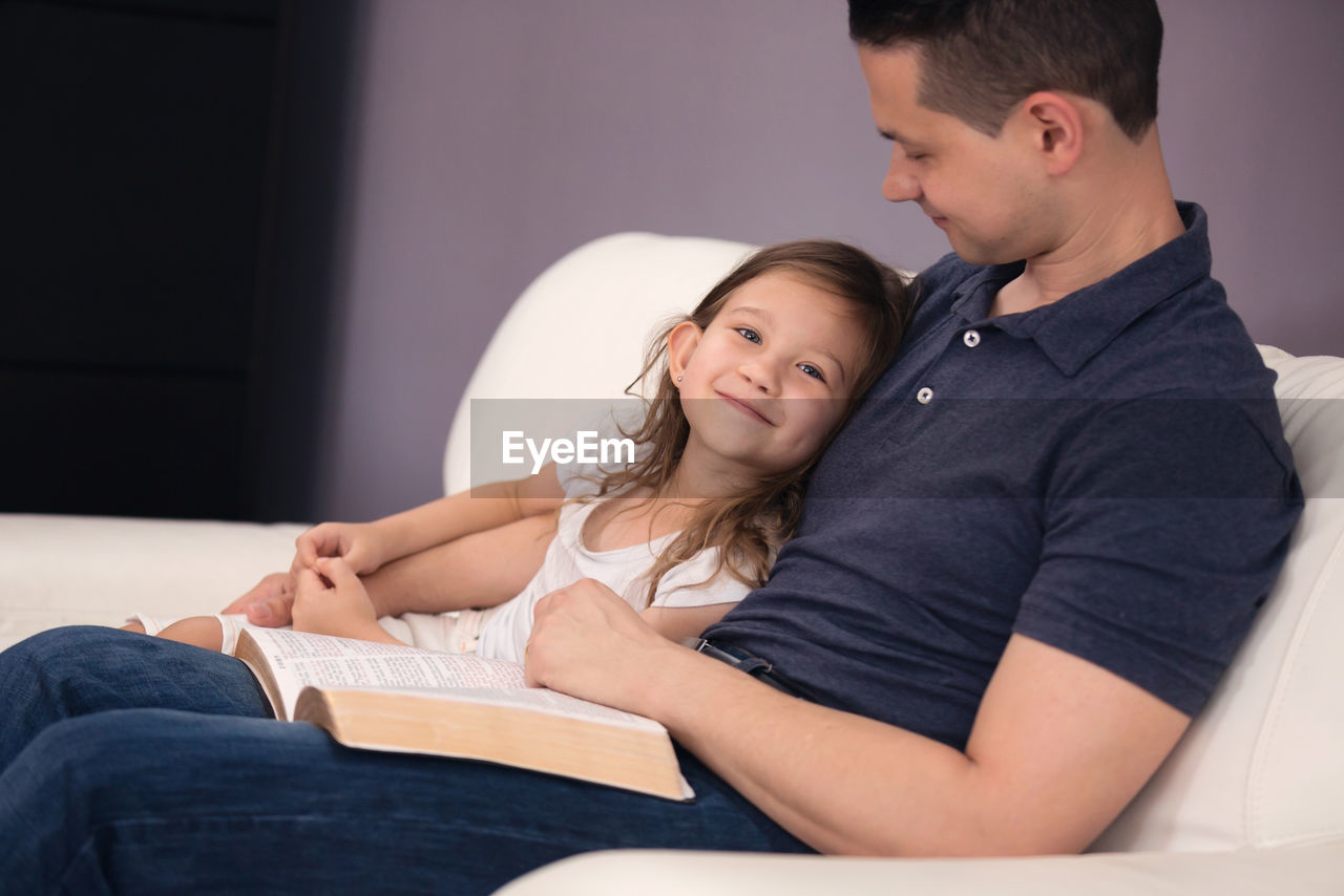 Father and daughter reading book on sofa at home