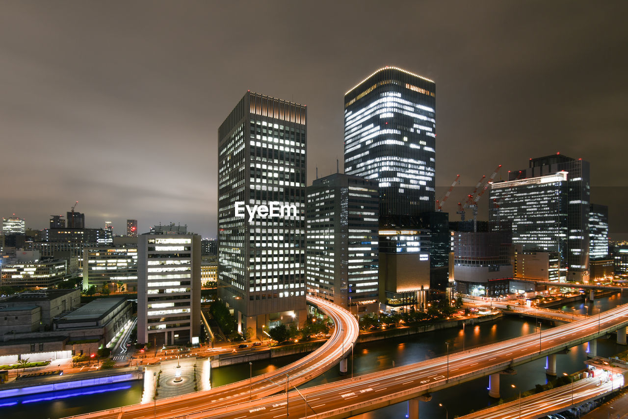 Illuminated modern buildings in city against sky at night