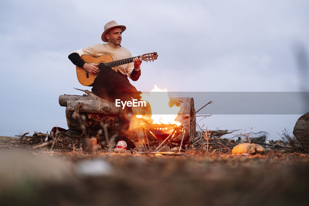 Mature man playing guitar against sky