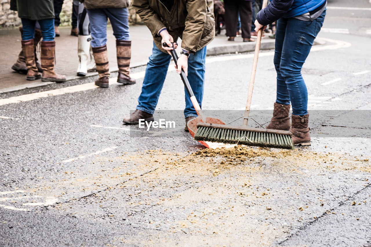Low section of people cleaning animal dung on road