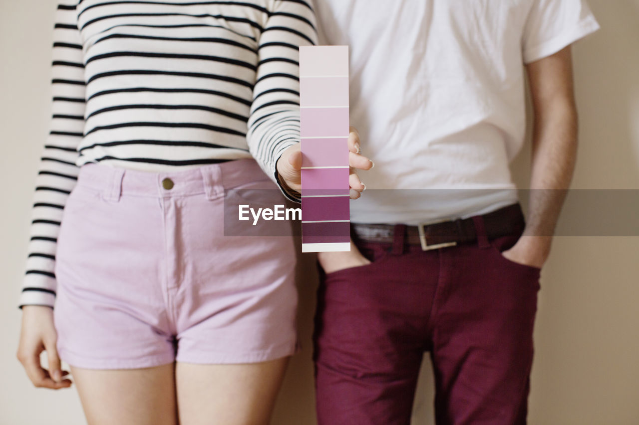 Midsection of woman holding color swatch while standing with man against wall at home