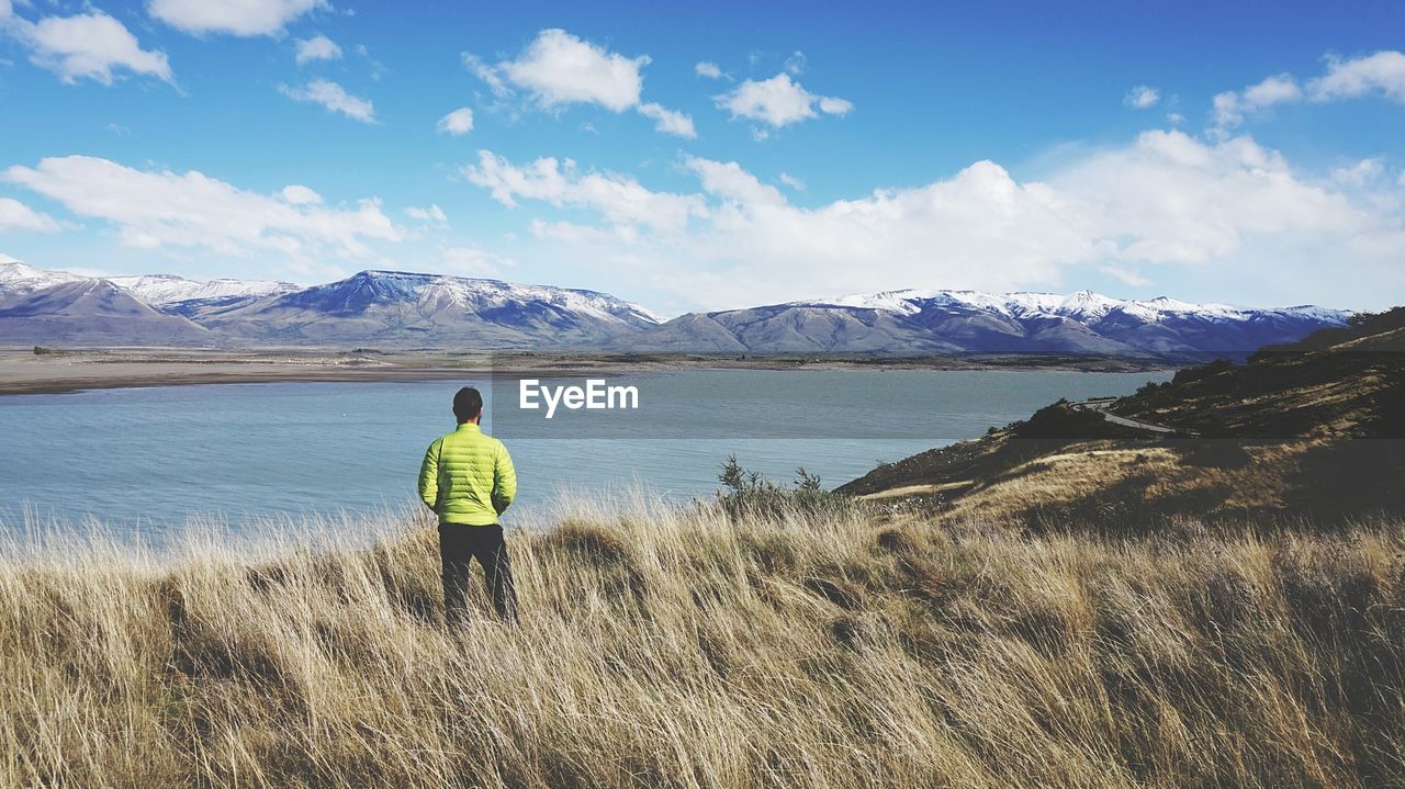 Rear view of man looking at sea against cloudy sky