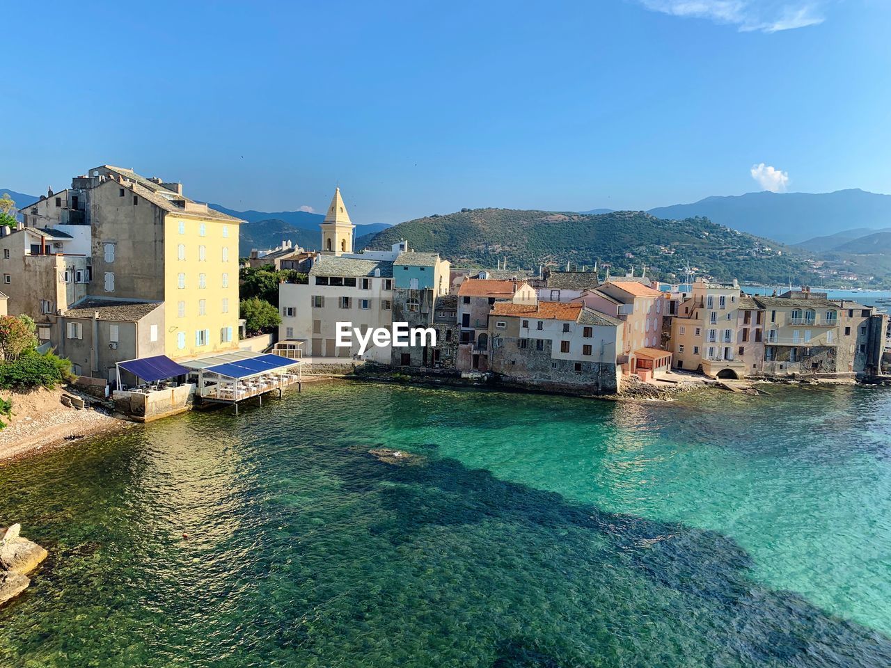 View of buildings by sea against blue sky