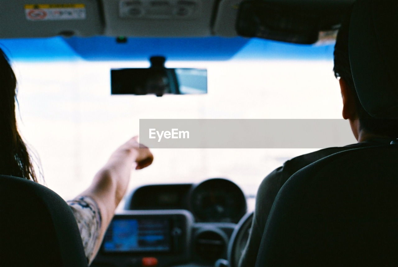 Rear view of man driving by woman pointing in car