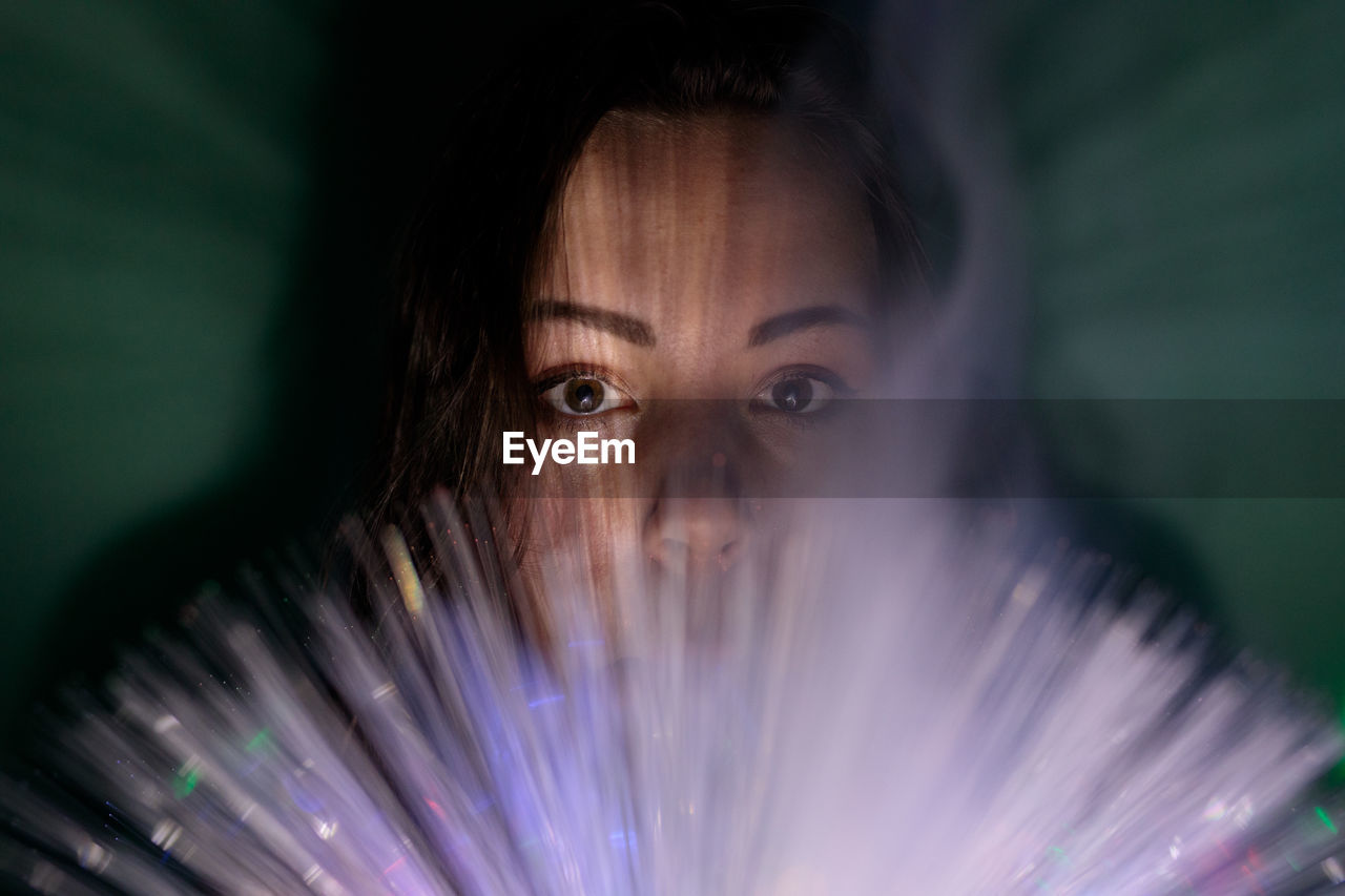 Close-up portrait of young woman holding multi colored fiber optic