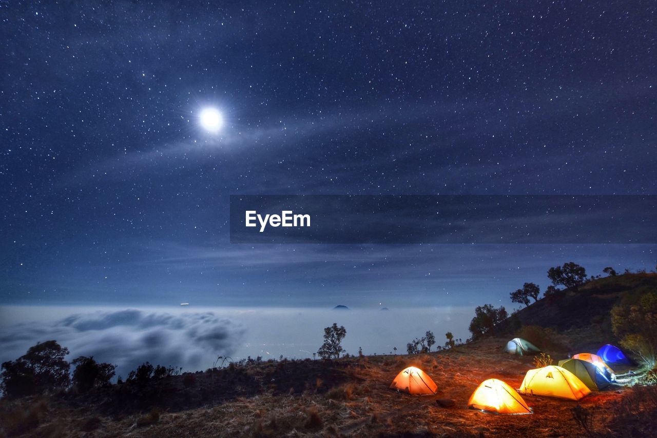 Illuminated tents on mountains against star field at night
