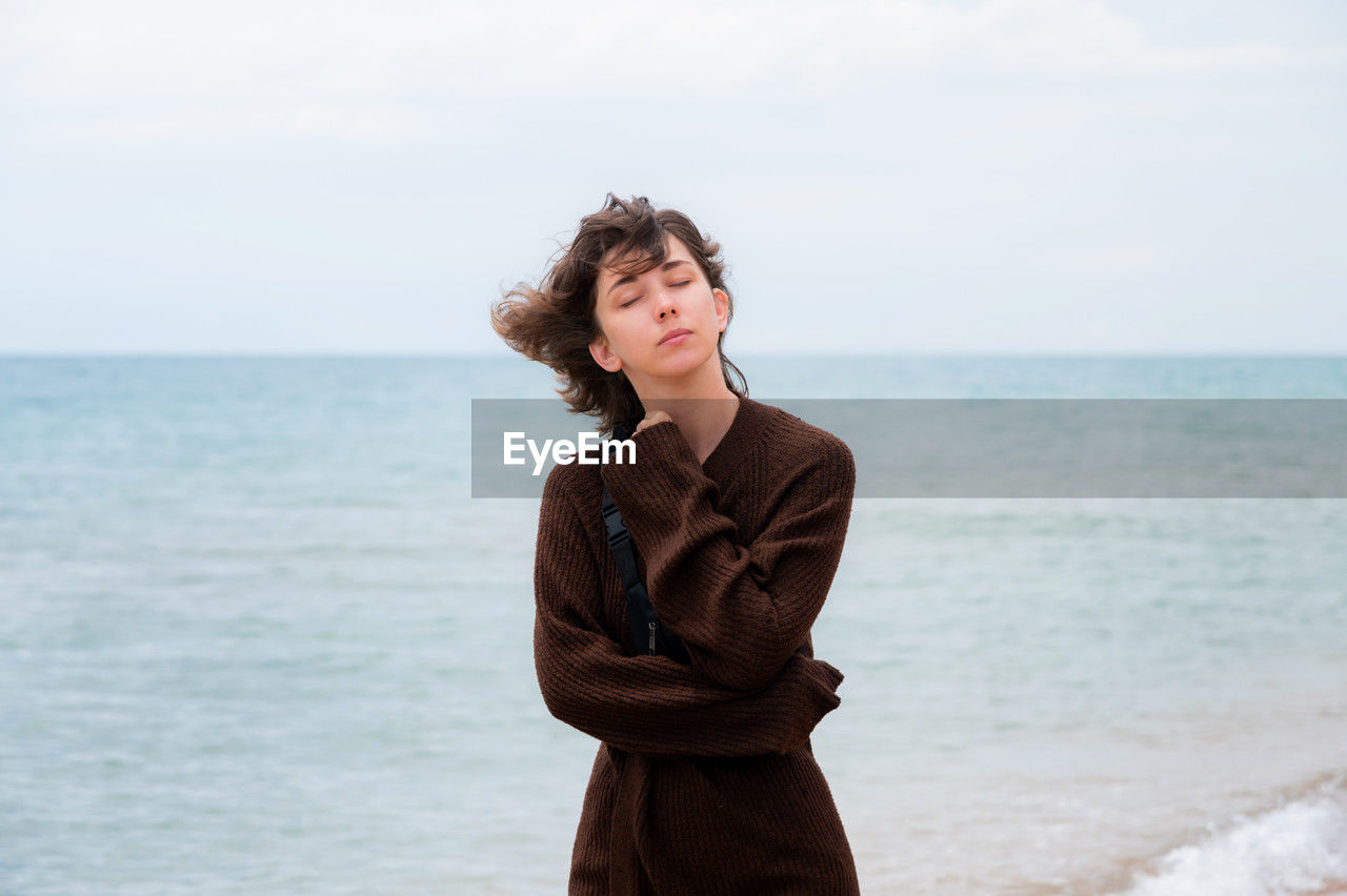 Portrait of carefree calm young caucasian woman in knitted rib sweater standing on sea in cold