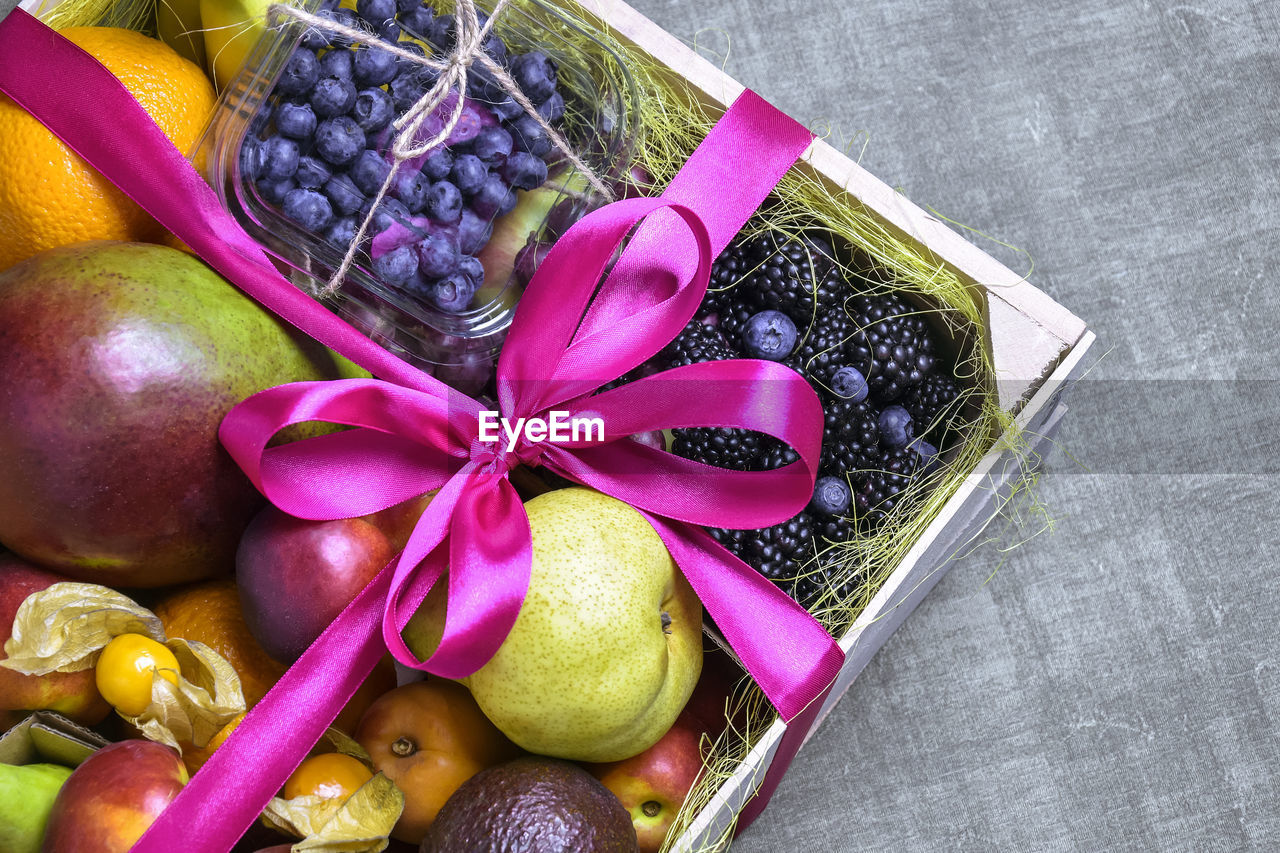 Juicy ripe fruits and berries are beautifully stacked in wooden box tied with ribbon. food delivery