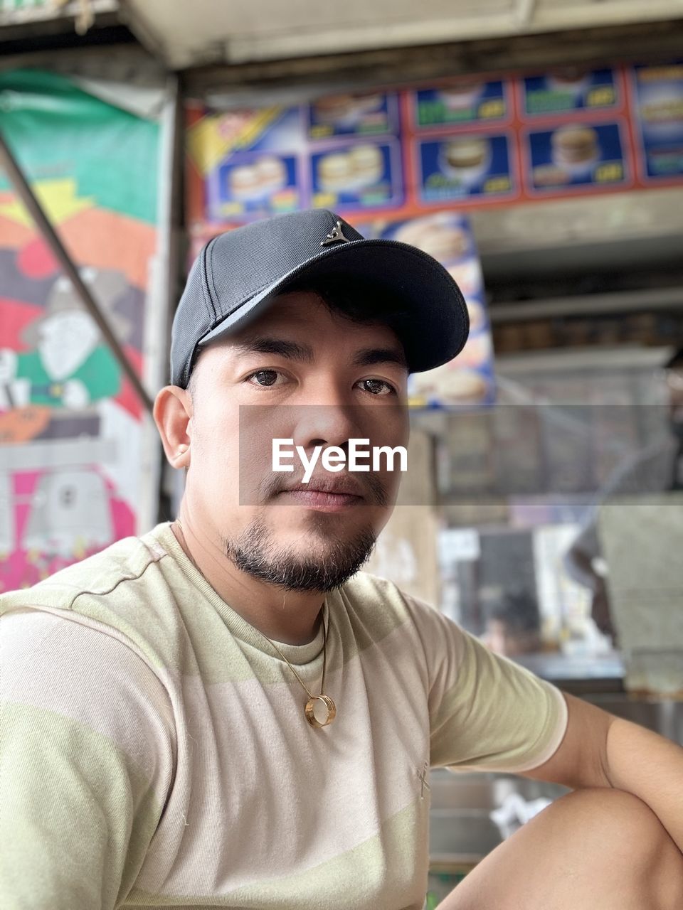 one person, portrait, young adult, adult, hat, looking at camera, men, cap, person, clothing, front view, beard, casual clothing, baseball cap, graffiti, sitting, day, fashion accessory, cool attitude, architecture, leisure activity, focus on foreground, looking, lifestyles, facial hair, city, headshot, serious, human face, outdoors