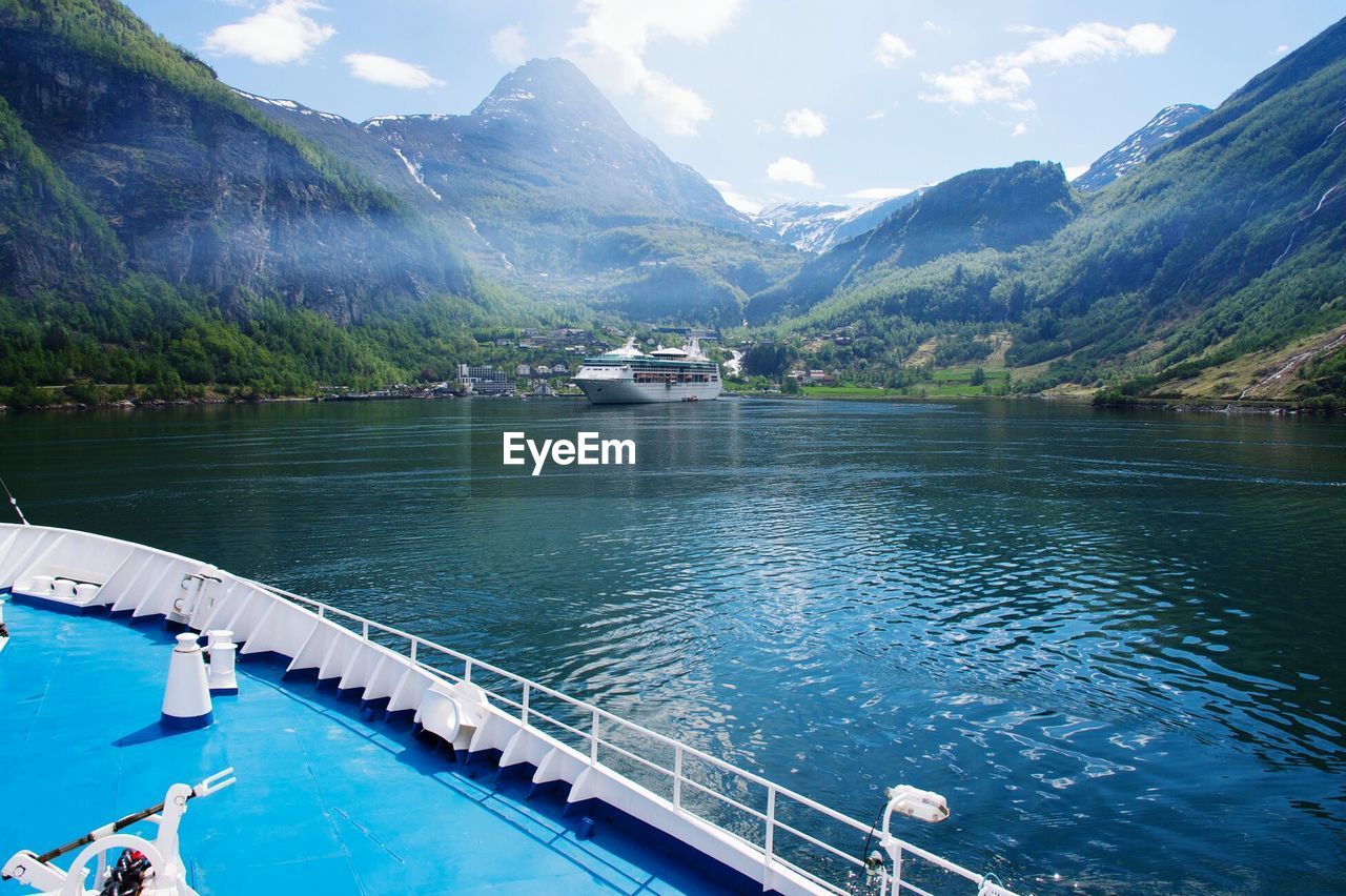 Cruise ships sailing on river by mountains against sky