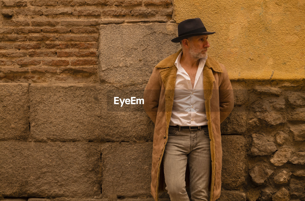 Adult man in coat standing in front of yellow and brick wall on street. madrid, spain