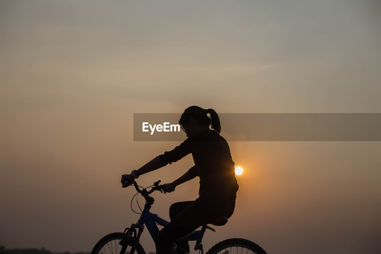 Silhouette woman riding bicycle against sky during sunset