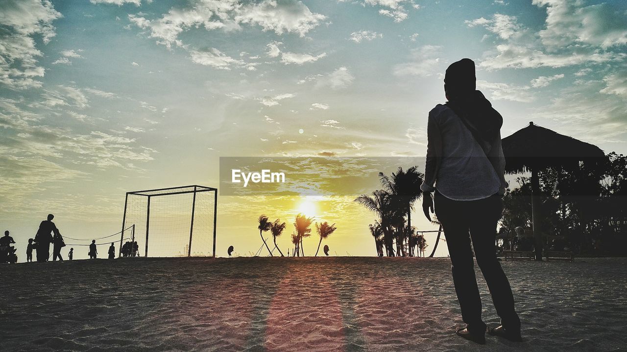 Rear view of woman standing on sand during sunset