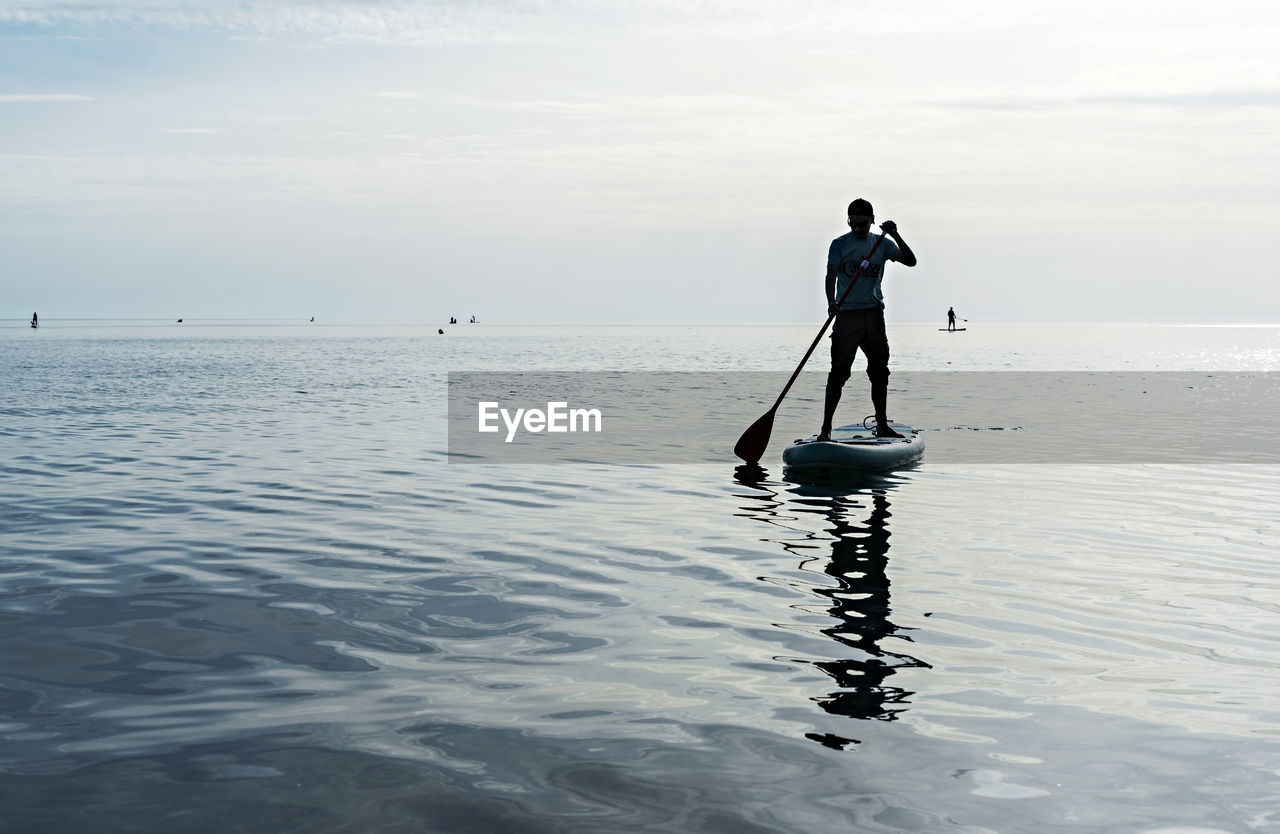 Young man on stand up paddle board on sea on sunny summer day, active lifestyle, outdoor activity