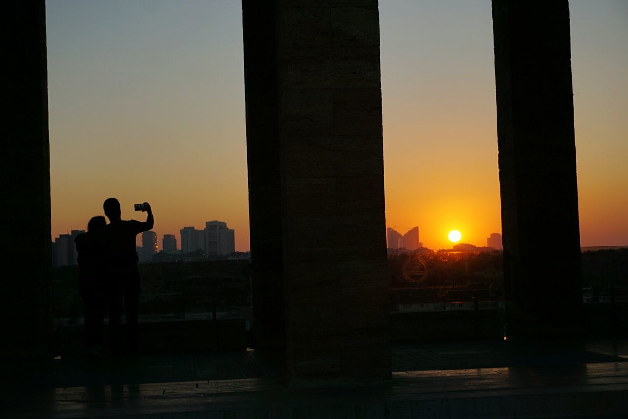 Silhouette man and woman taking selfie against sky during sunset