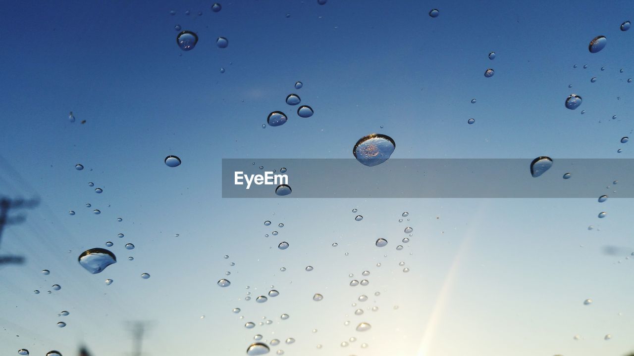 Close-up of water drops on glass against sky