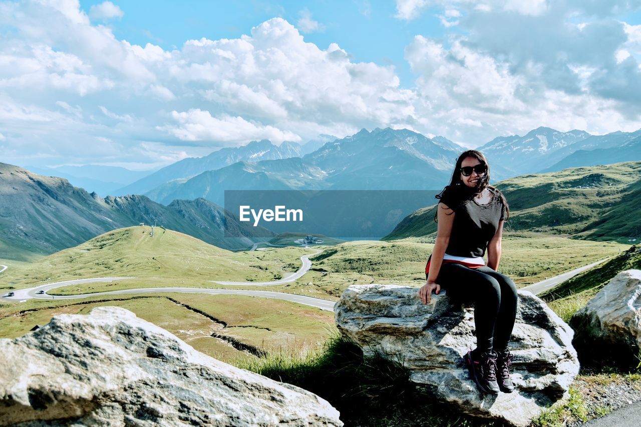 Young woman sitting on mountain against sky