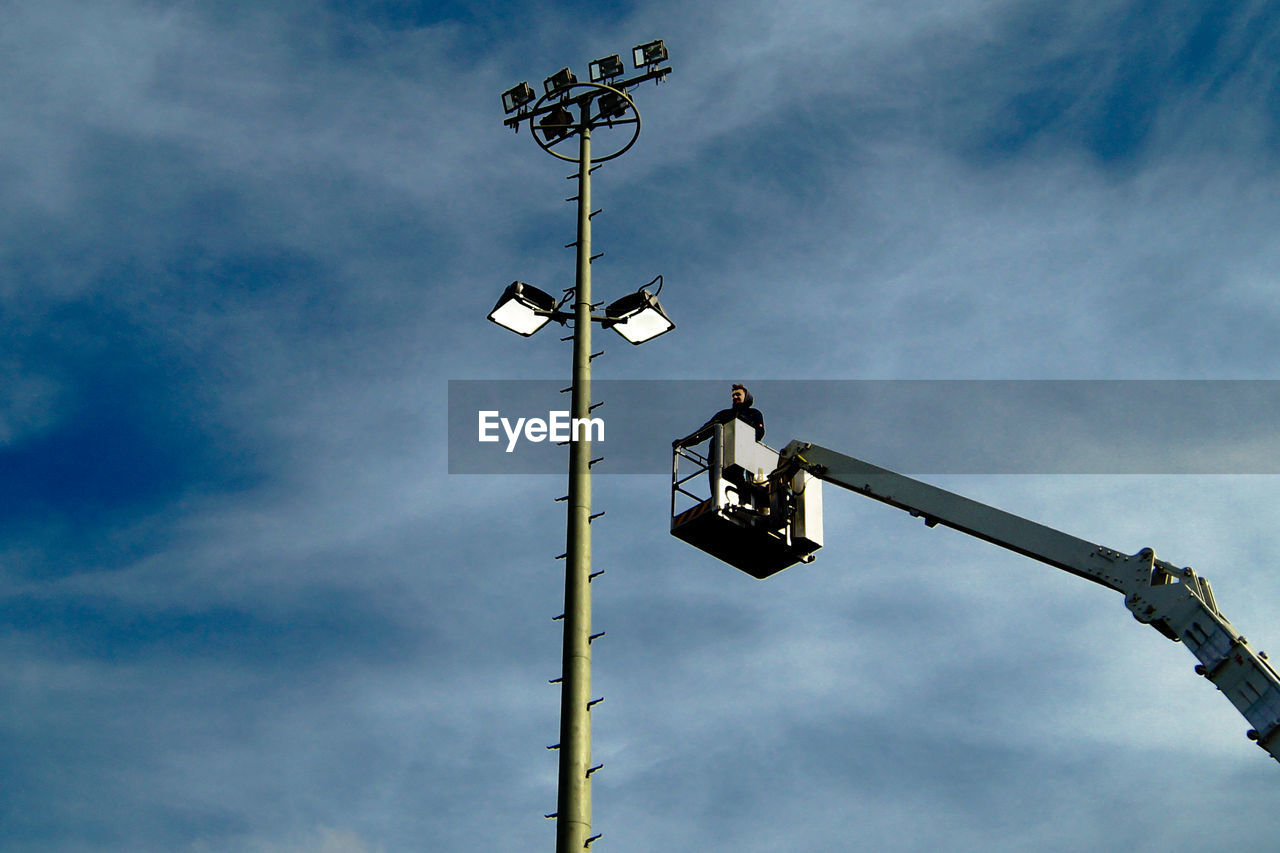 Maintenance engineer on cherry picker reaching towards floodlight