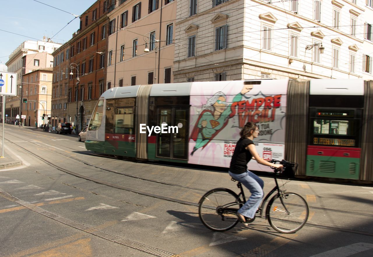 MAN RIDING BICYCLE ON ROAD AGAINST BUILDINGS