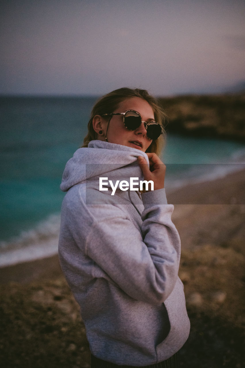 Side view of woman wearing sunglasses standing by sea