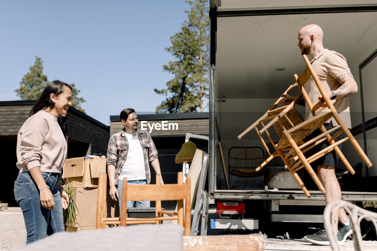 Couple looking at mover unloading chairs from truck on sunny day