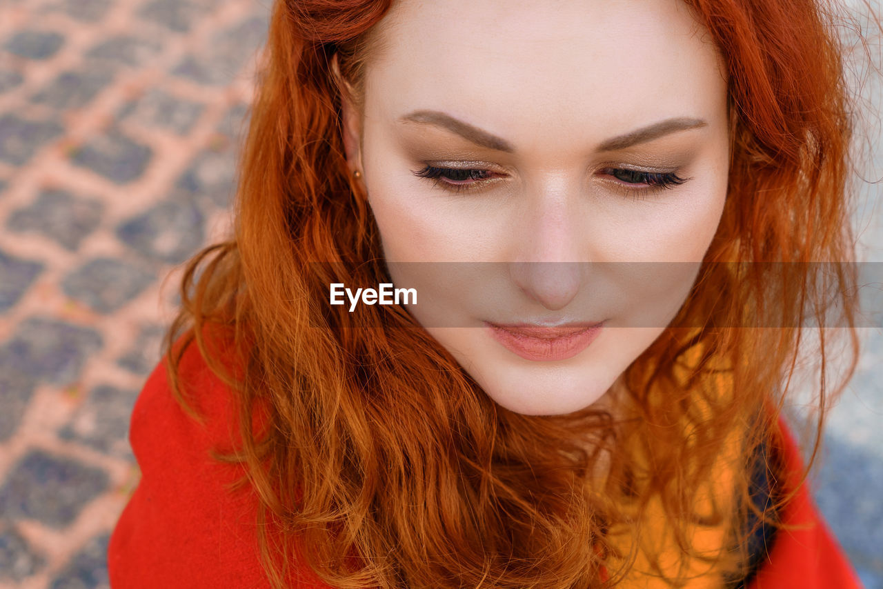 Close-up portrait young caucasian woman with red curly hair in a red coat