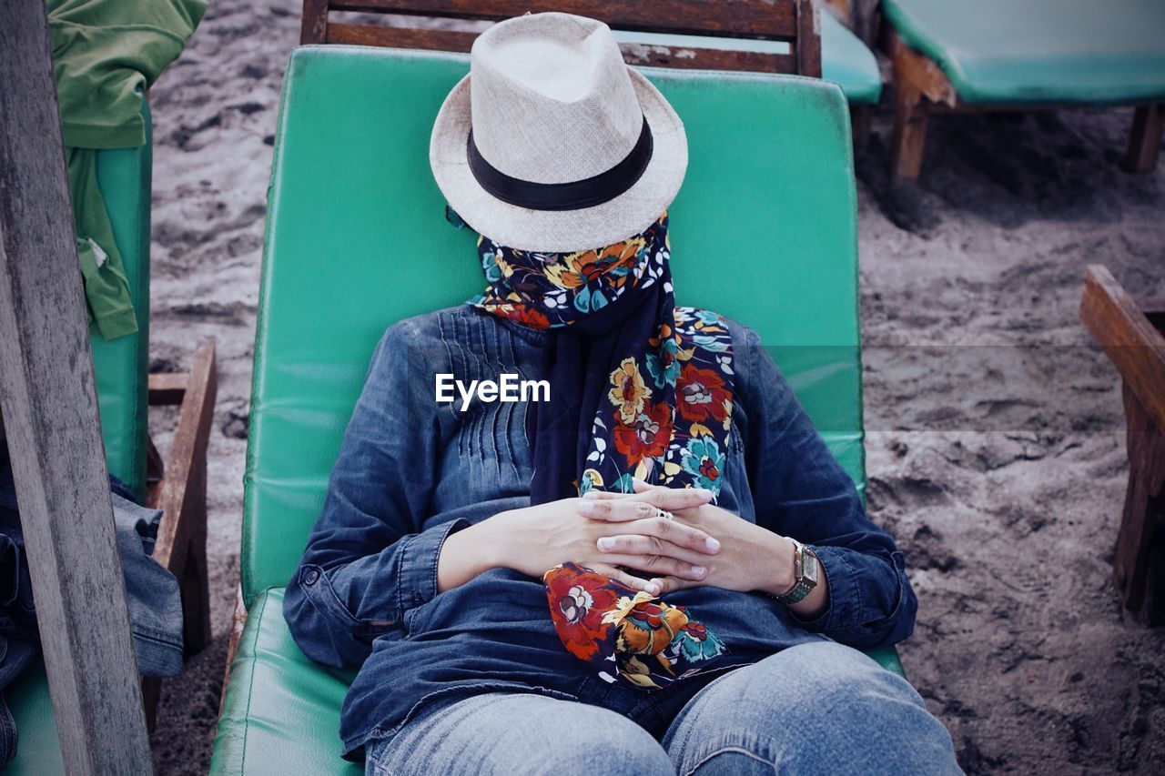 High angle view of woman face covered with hat while lying on lounge chair