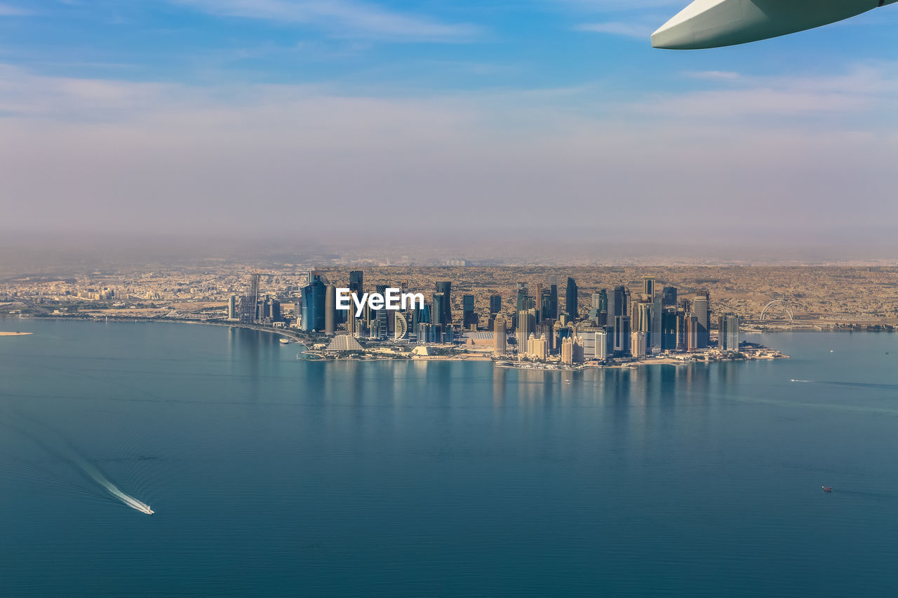 Aerial view of city by sea against cloudy sky