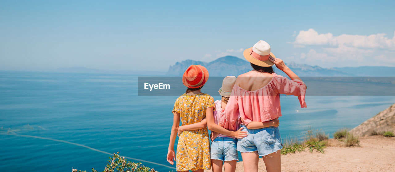 REAR VIEW OF WOMEN WITH UMBRELLA AGAINST SEA