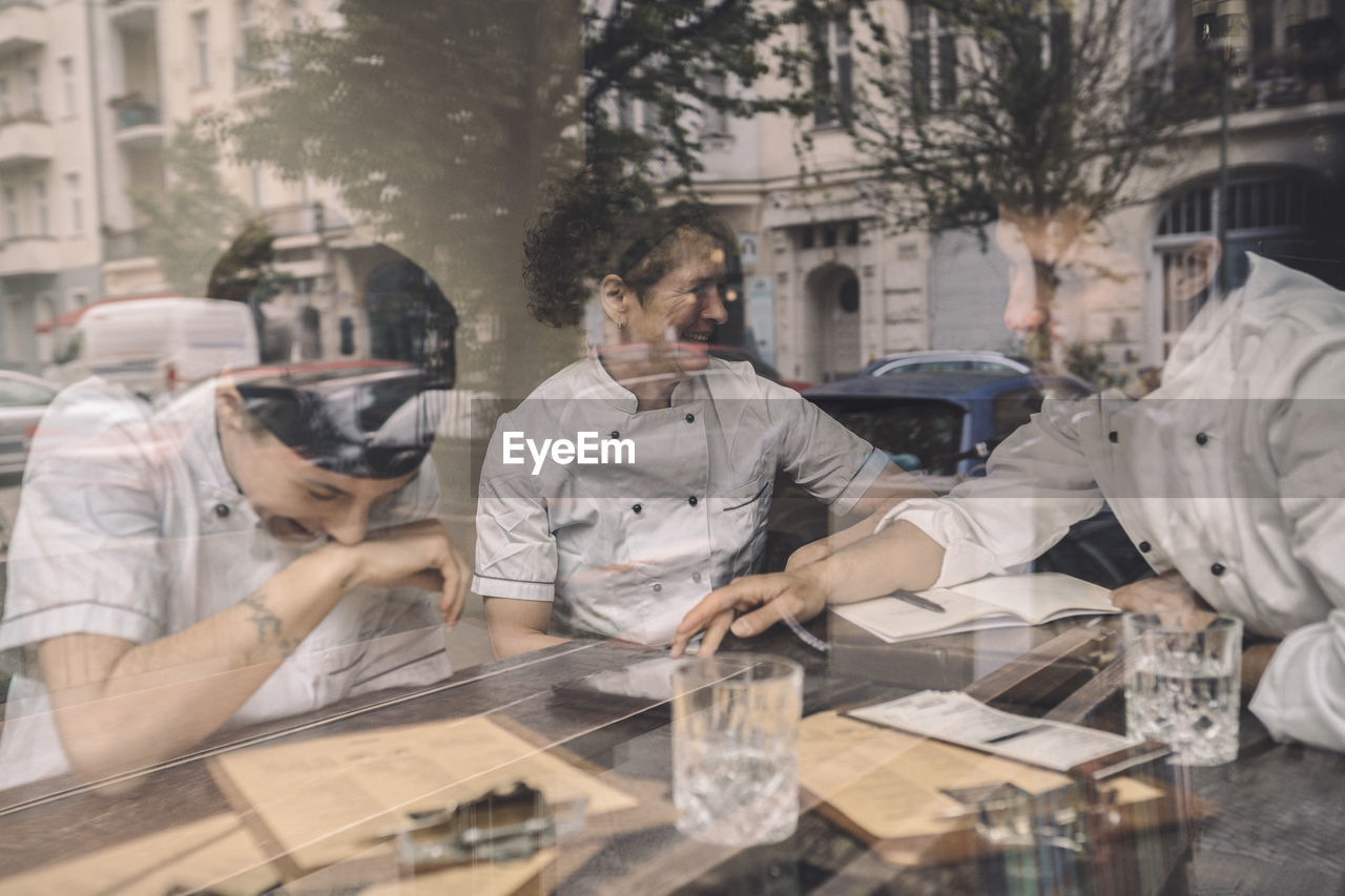 Happy coworkers sitting at restaurant table seen through glass window