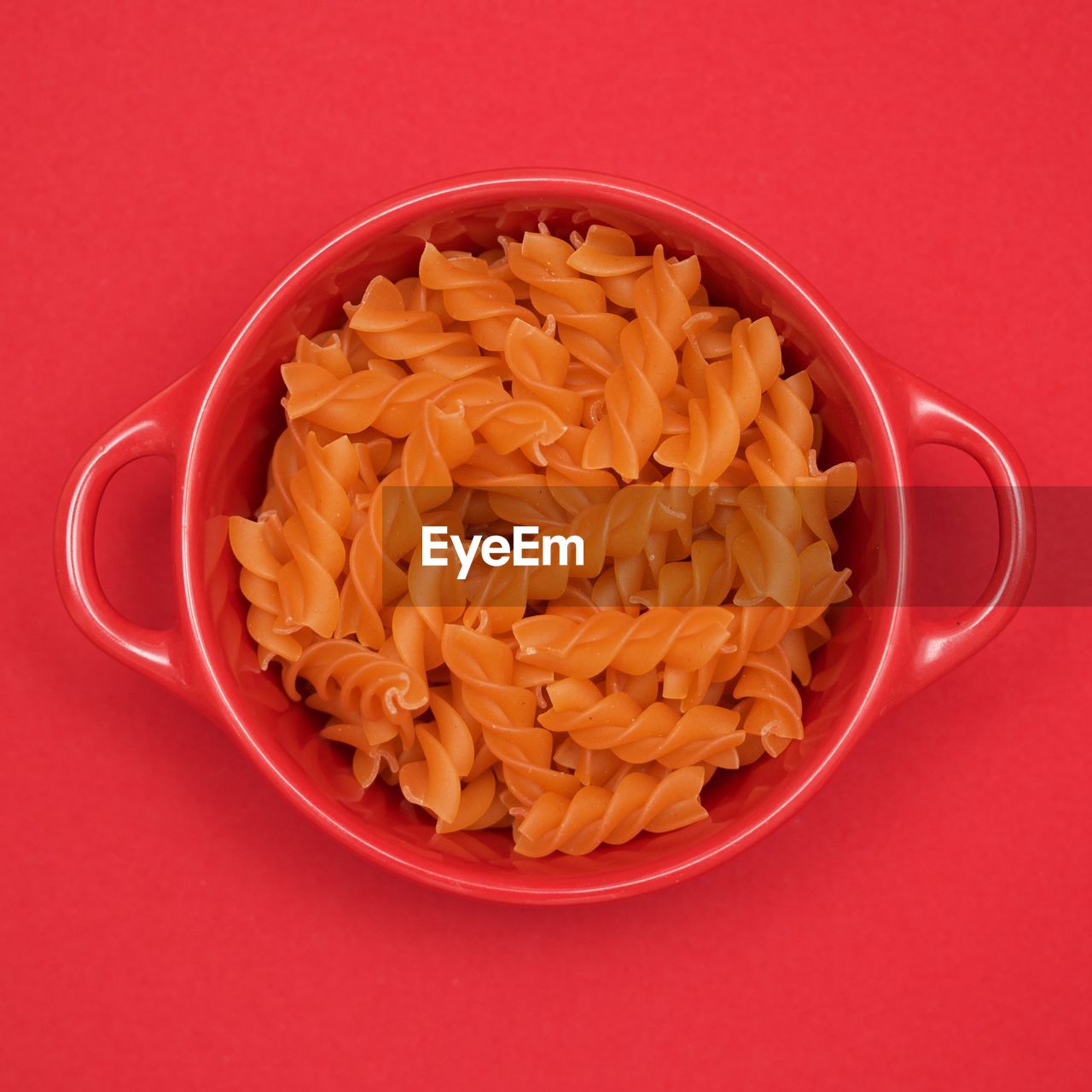 Red fusilli in a red bowl on red background