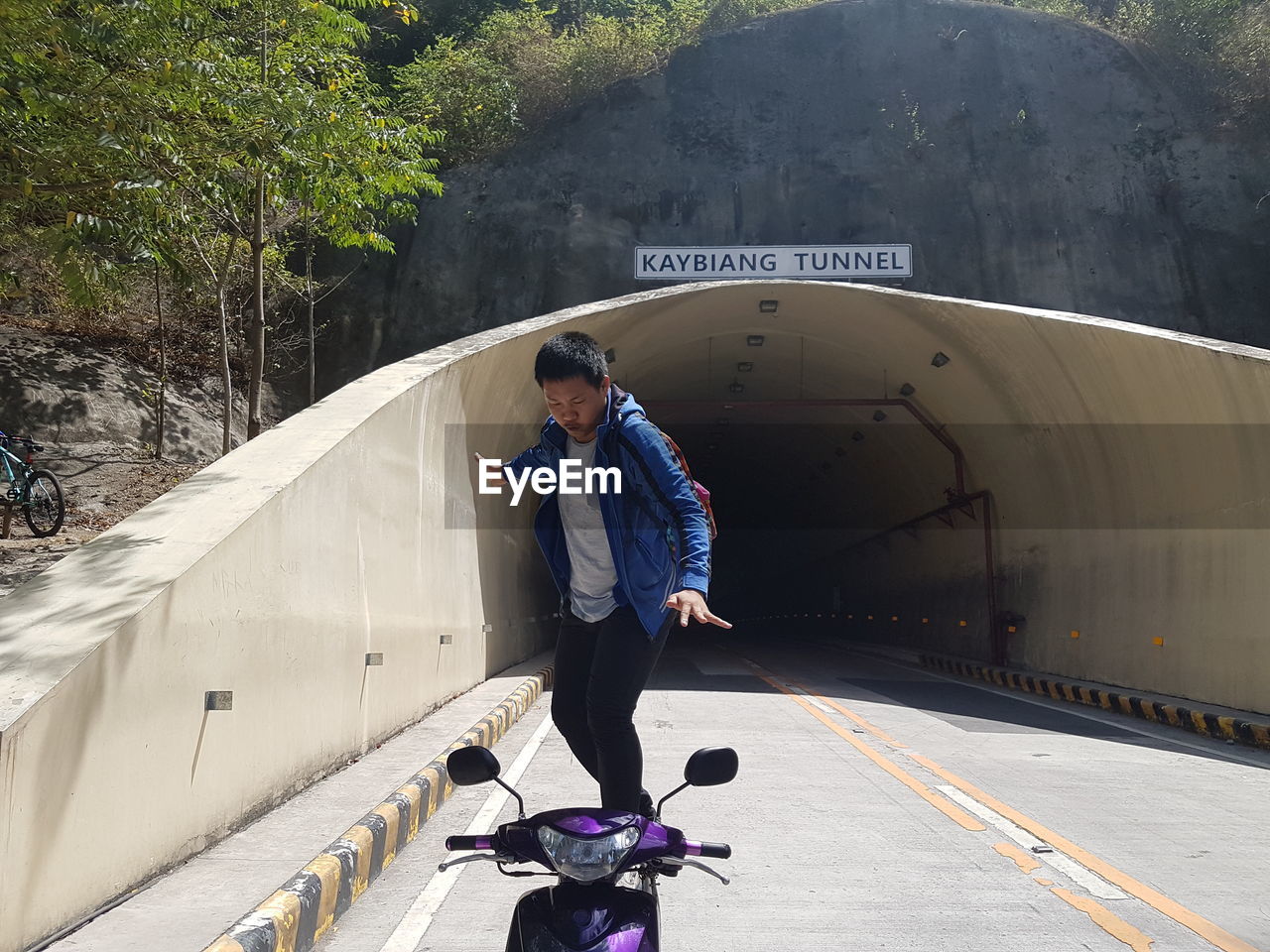 Full length of man balancing on scooter against tunnel by trees