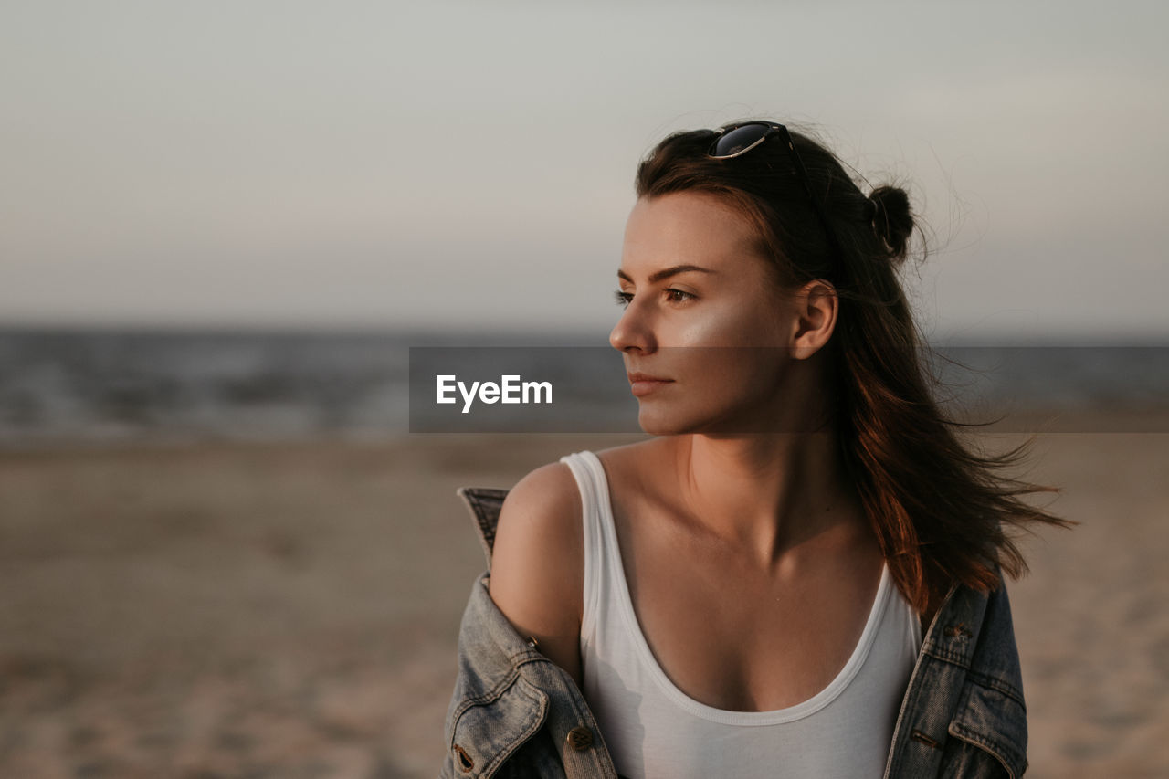 Close-up of young woman against sea during sunset