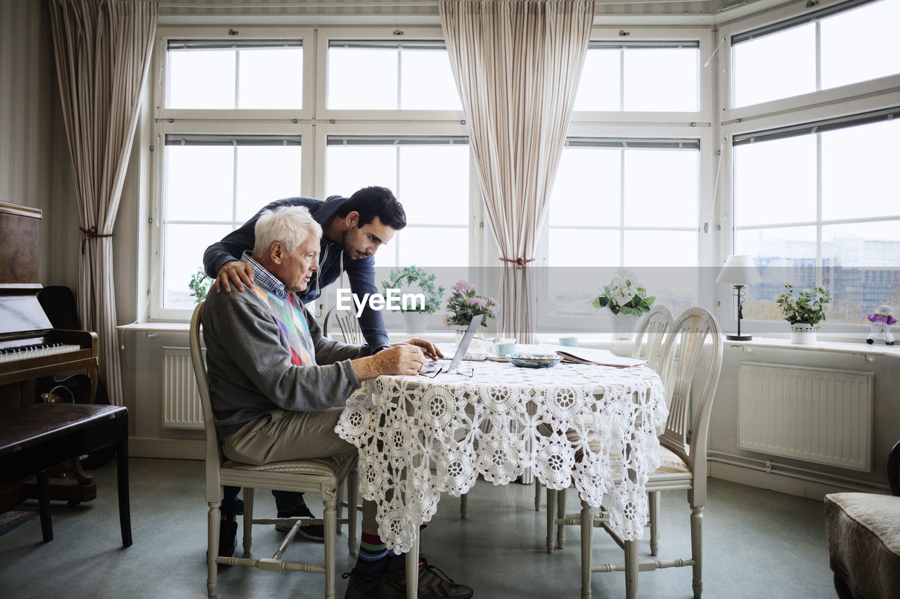 Senior man using laptop with caretaker at nursing home