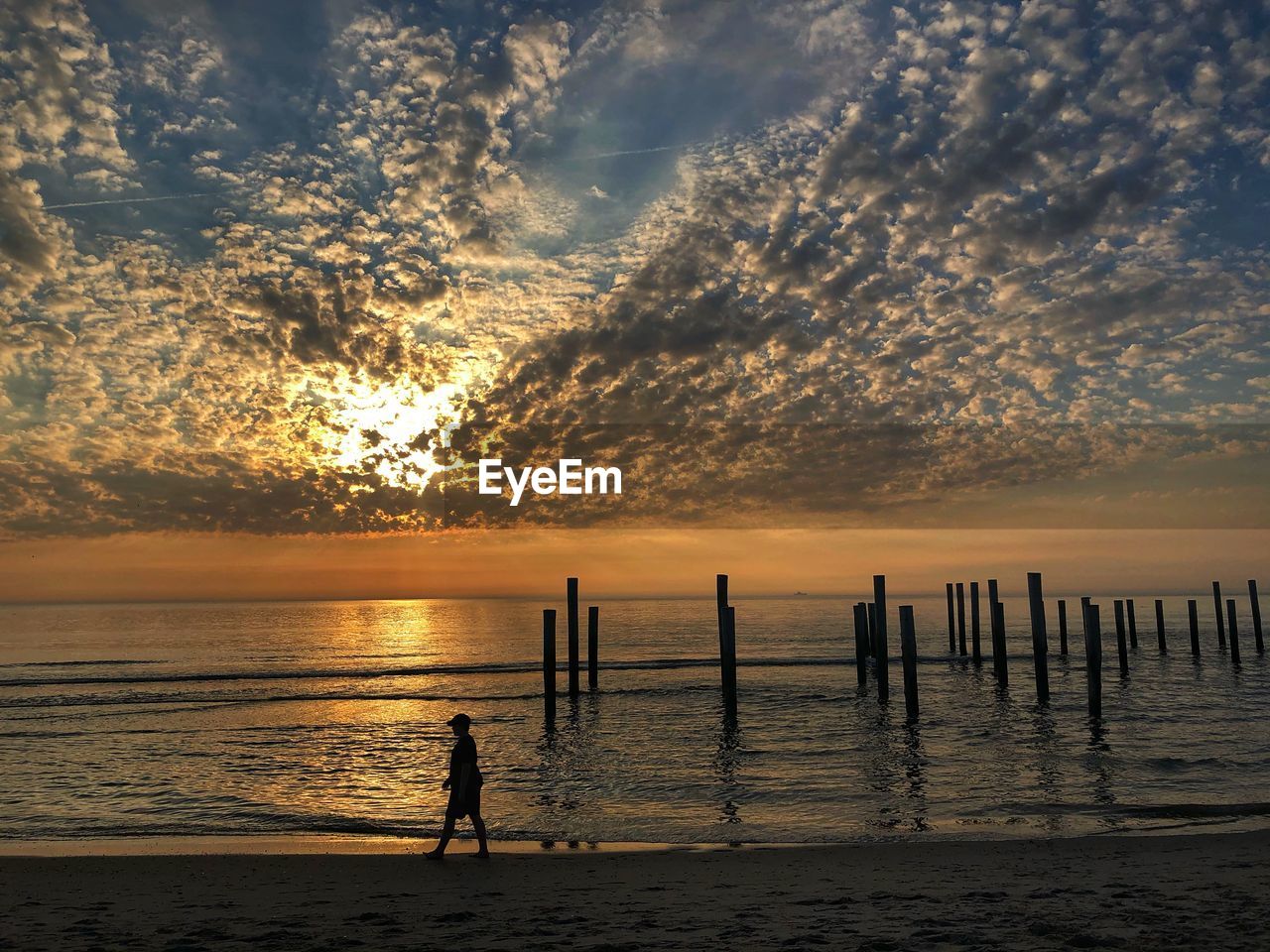 SILHOUETTE MAN STANDING ON WOODEN POST IN SEA DURING SUNSET