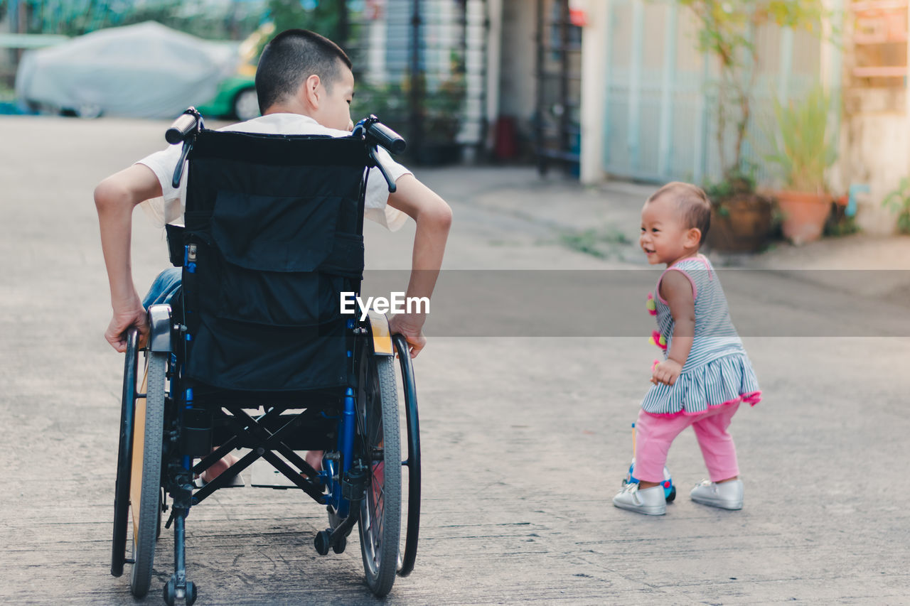 Rear view of brother on wheelchair with sister outdoors