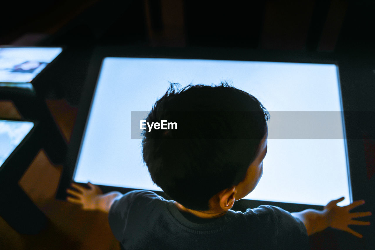 Rear view of boy standing by device screen