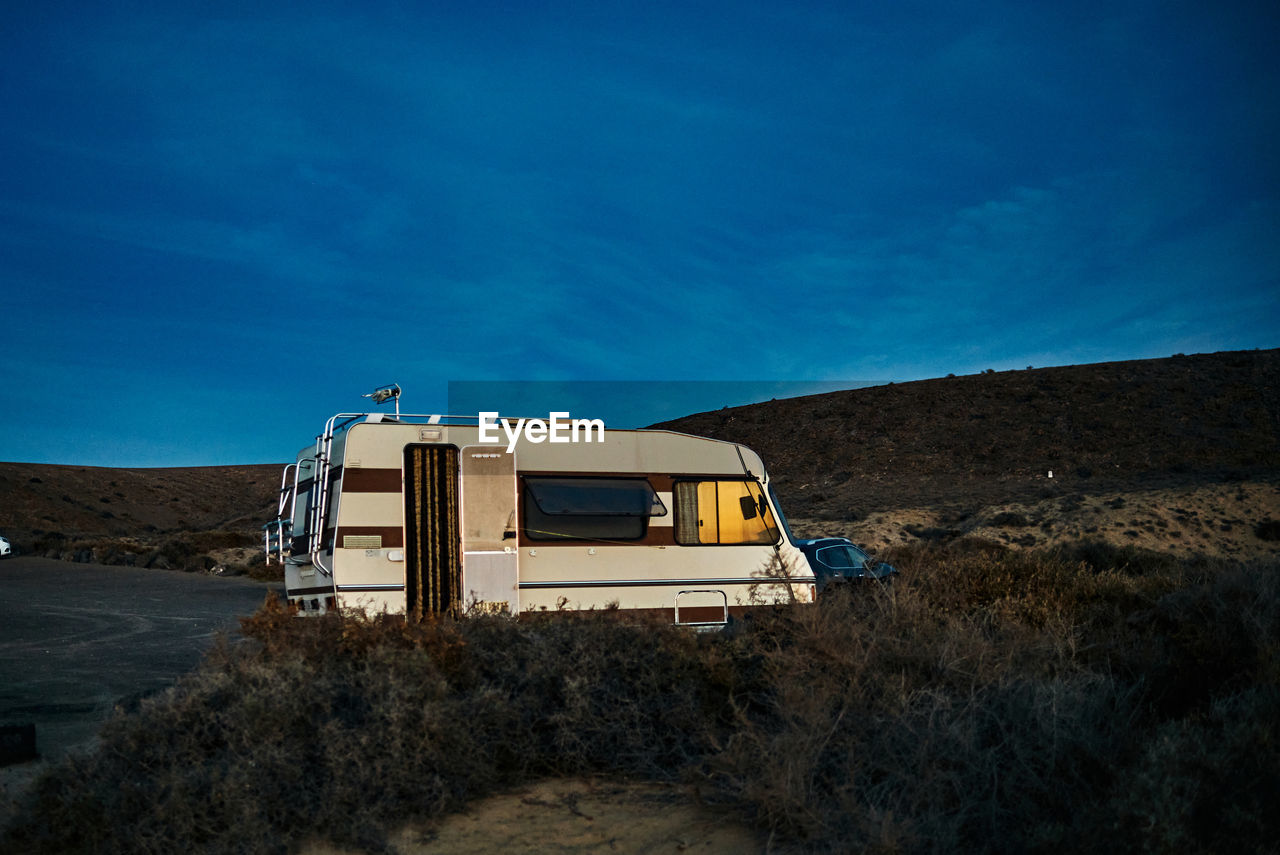 Vintage camper with opened door parked near hills against blue sky in evening in fuerteventura, spain