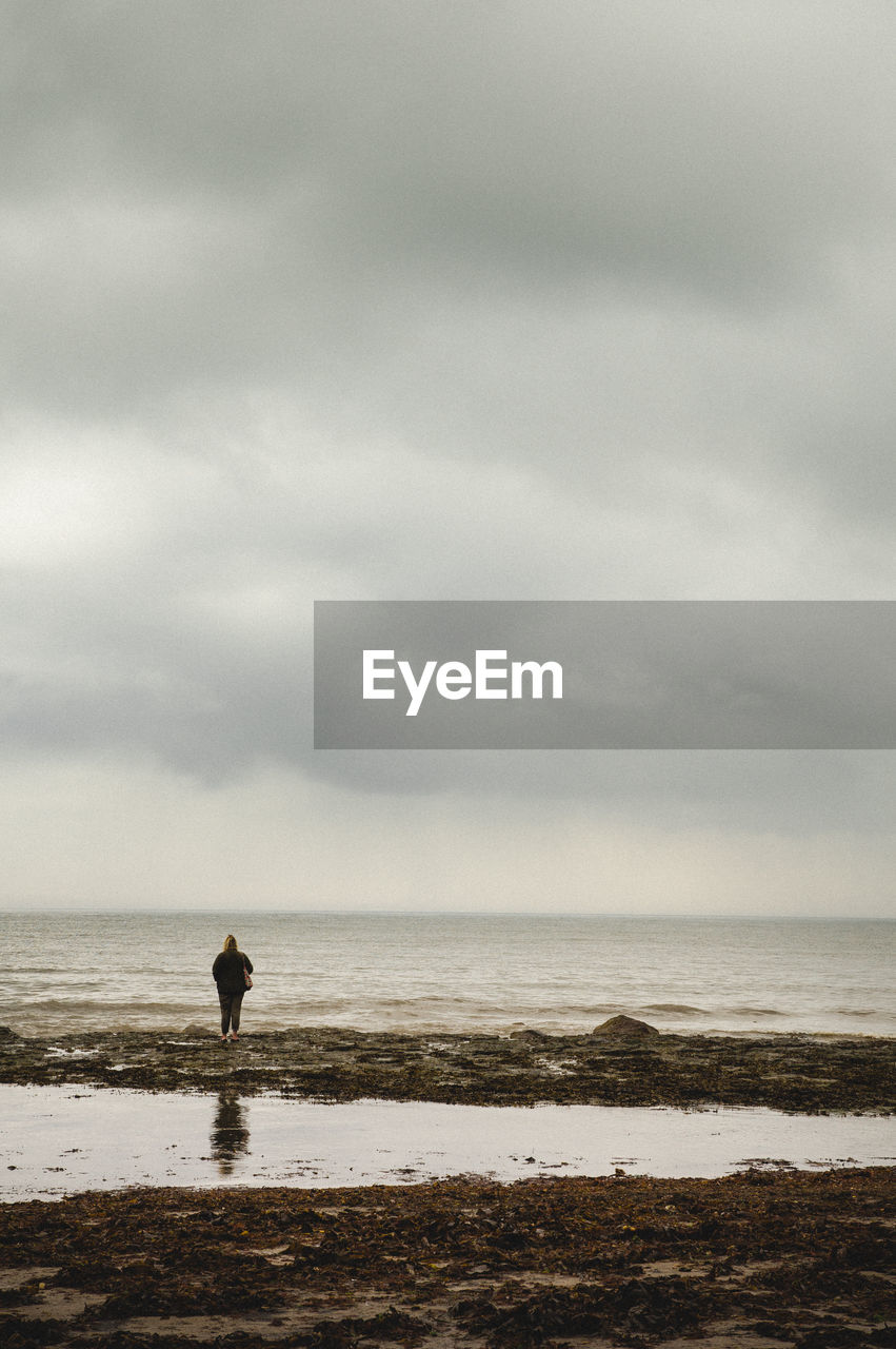 Rear view of woman at calm sea against cloudy sky