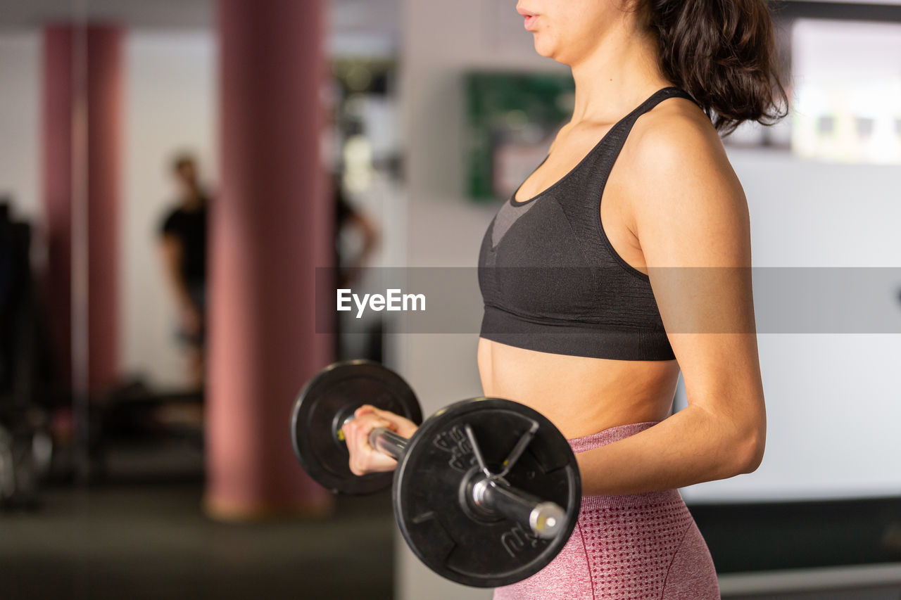 midsection of woman lifting dumbbell at gym