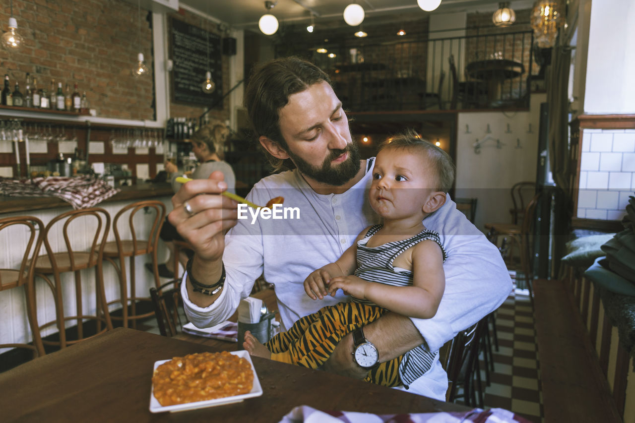 Mid adult man feeding baby boy at restaurant table