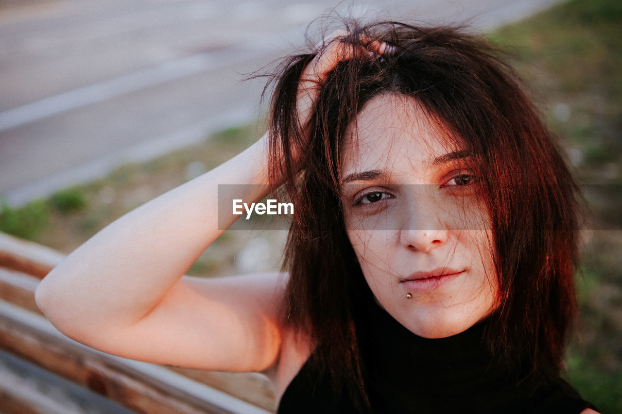 Close-up portrait of young woman with hand in hair outdoors