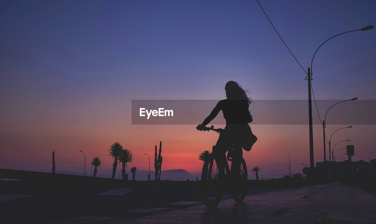 Silhouette woman jumping on street against sky during sunset