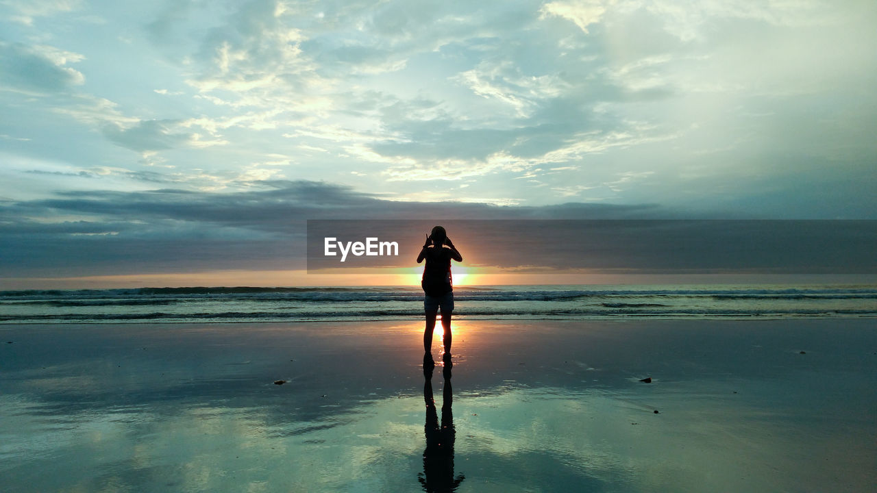 Rear view of woman standing on beach against sky during sunset