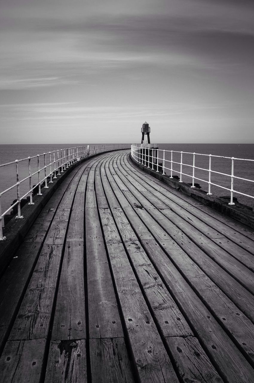 Empty boardwalk at sea against sky