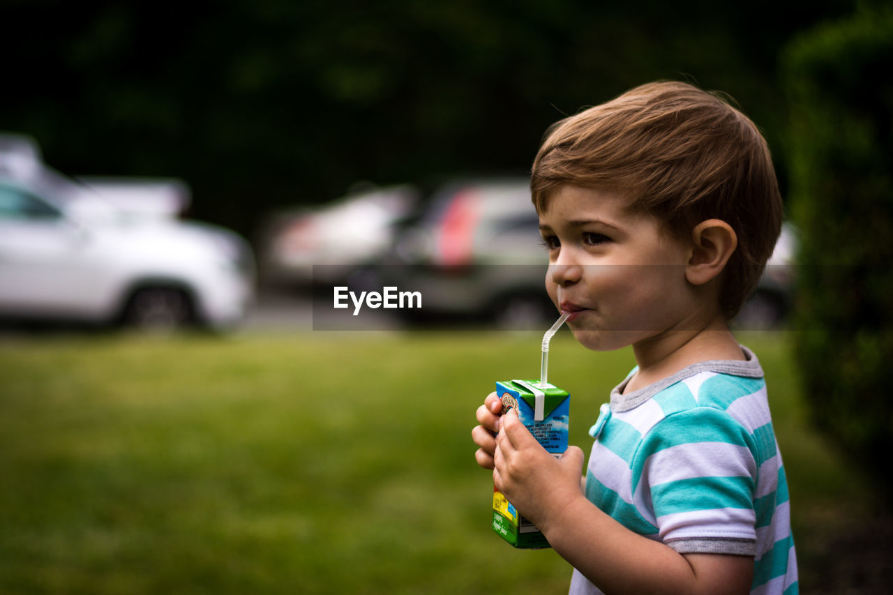 Side view of boy having drink while standing on field