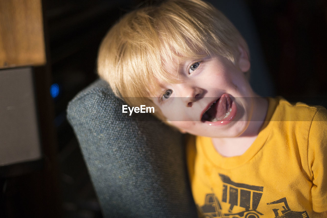 Portrait of boy sticking out tongue while leaning on sofa at home