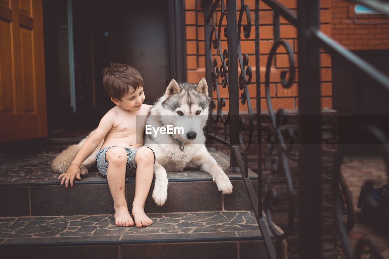 Cute shirtless boy sitting with german shepherd on steps