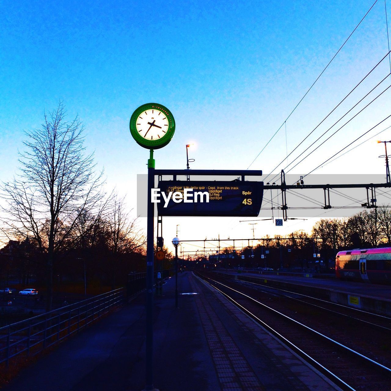 Illuminated clock and signboard on railroad station against sky during sunset