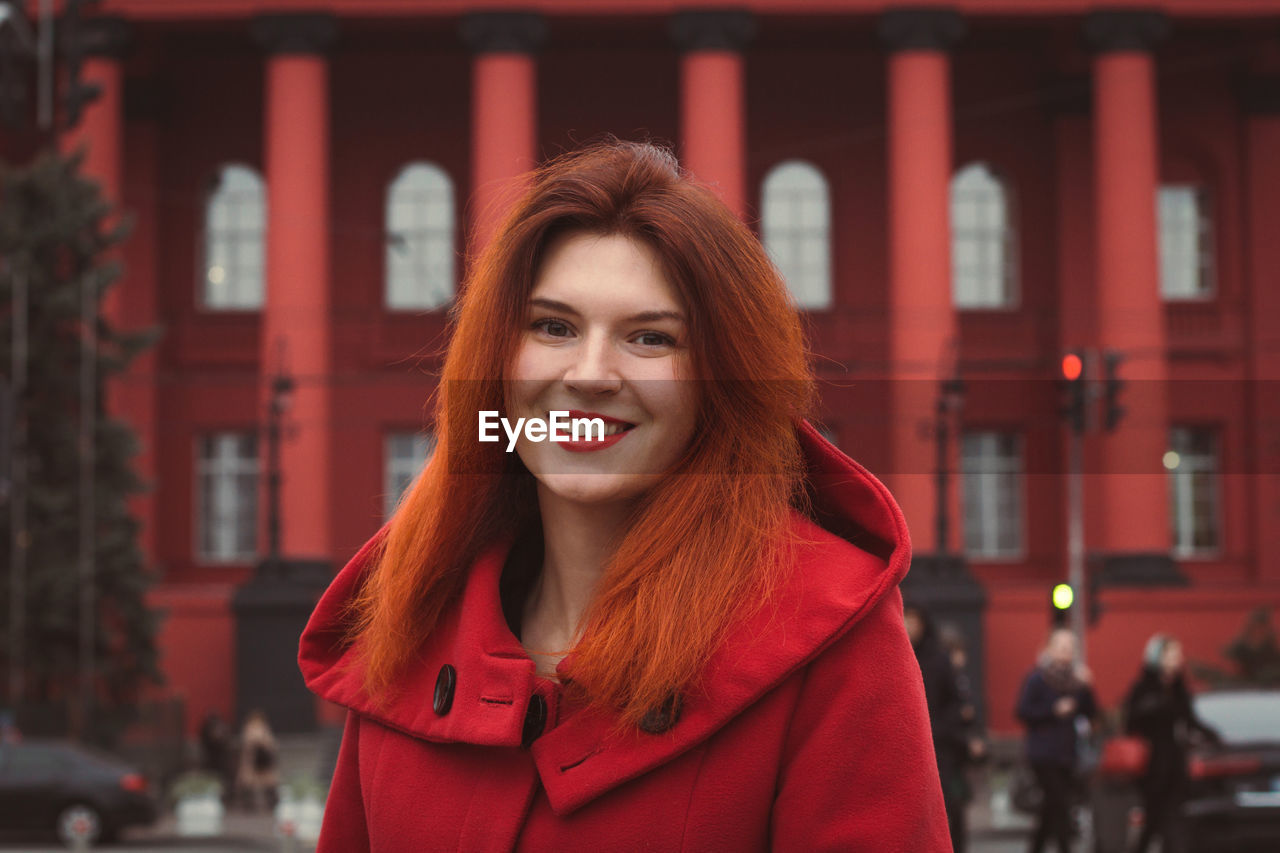 Close up young smiling woman in red coat on street portrait picture